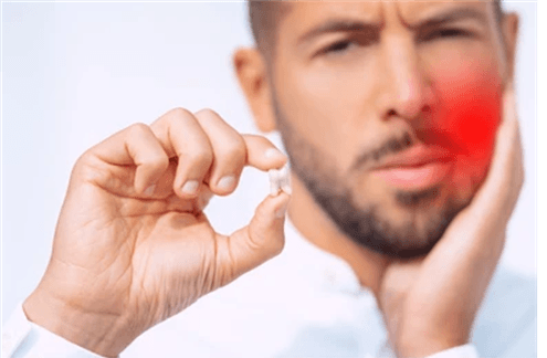 Picture2 | Neo Dental | Neo Dental Man with a red cheek rests his head in one hand while holding a pill near his mouth, about to take it for pain relief.
