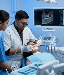 Picture5 | Neo Dental | Neo Dental Dentist and assistant treating a patient in a dental chair as a monitor shows a dental X-ray image of teeth.