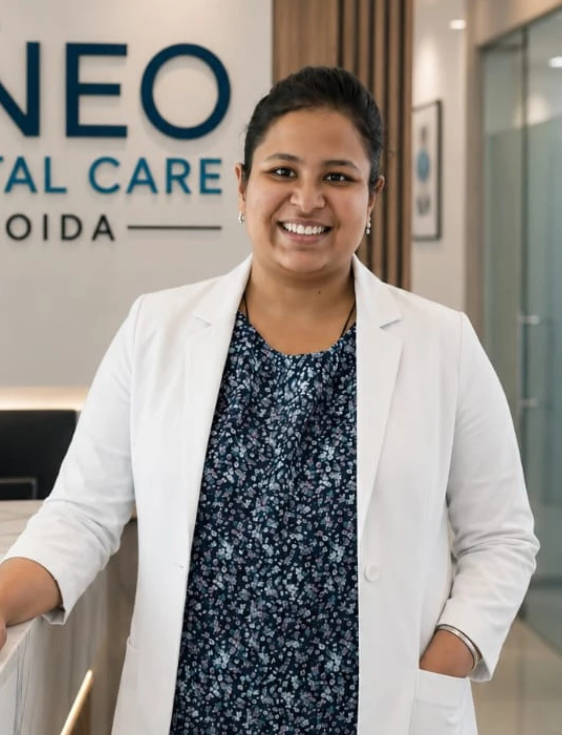 3 | Neo Dental | Neo Dental Smiling female clinician in a white coat standing in a dental clinic reception area with a sign in the background.